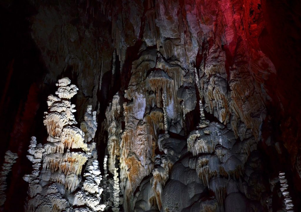 Groepsfoto kampeerders bij ingang van een grotte in de Belgische Ardennen met groen berglandschap